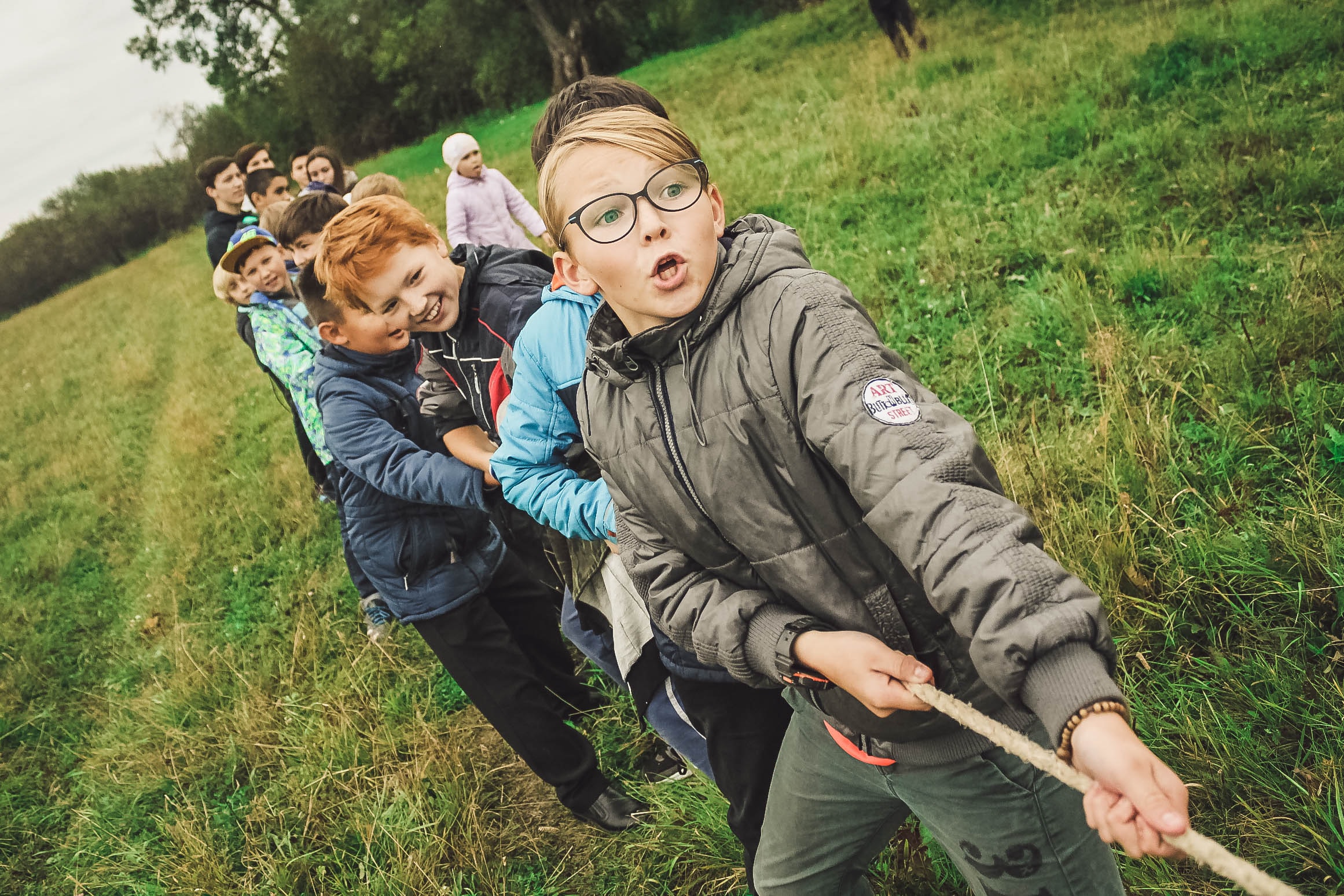 Skupina detí hrá hru na ťahanie lana na čerstvom vzduchu v prírode.